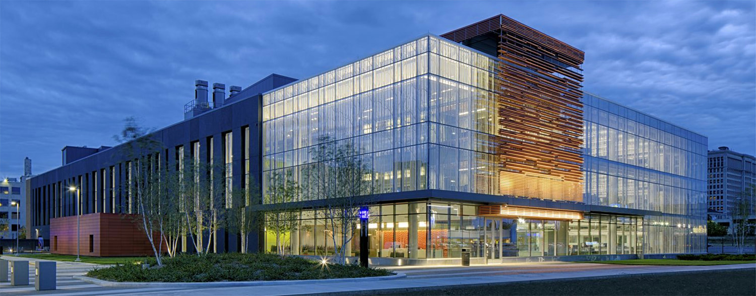The Integrative Biosciences Center at Wayne State, home of the Institute of Environmental Health Sciences and our lab. A glass paneled, artistic building, lit up at dusk.